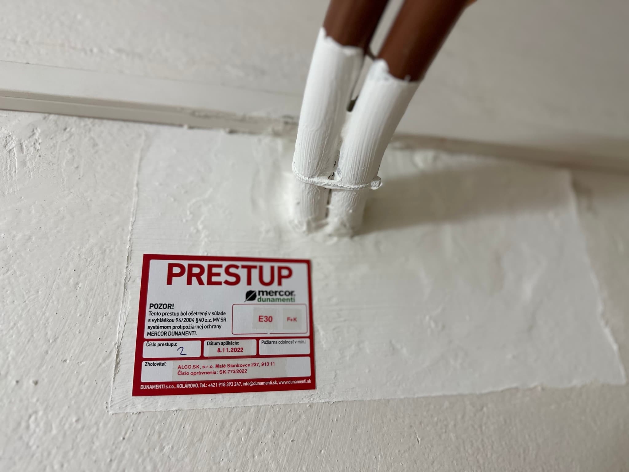 Certifikovaný požiarny prestup – dve potrubia cez stenu, pečatené protipožiarnou hmotou, štítok MERCOR DUNAMENTI E30. ALCO.SK.